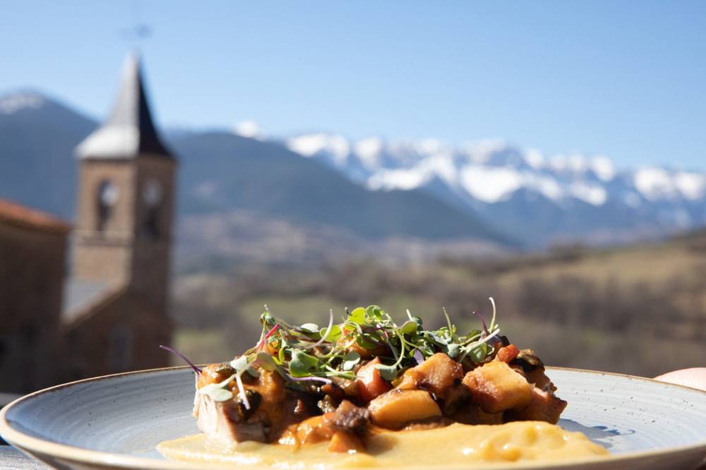 Plated dish held up with the village church and snowy peaks behind